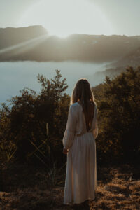 Woman Standing on hill overlooking water as sun sets
