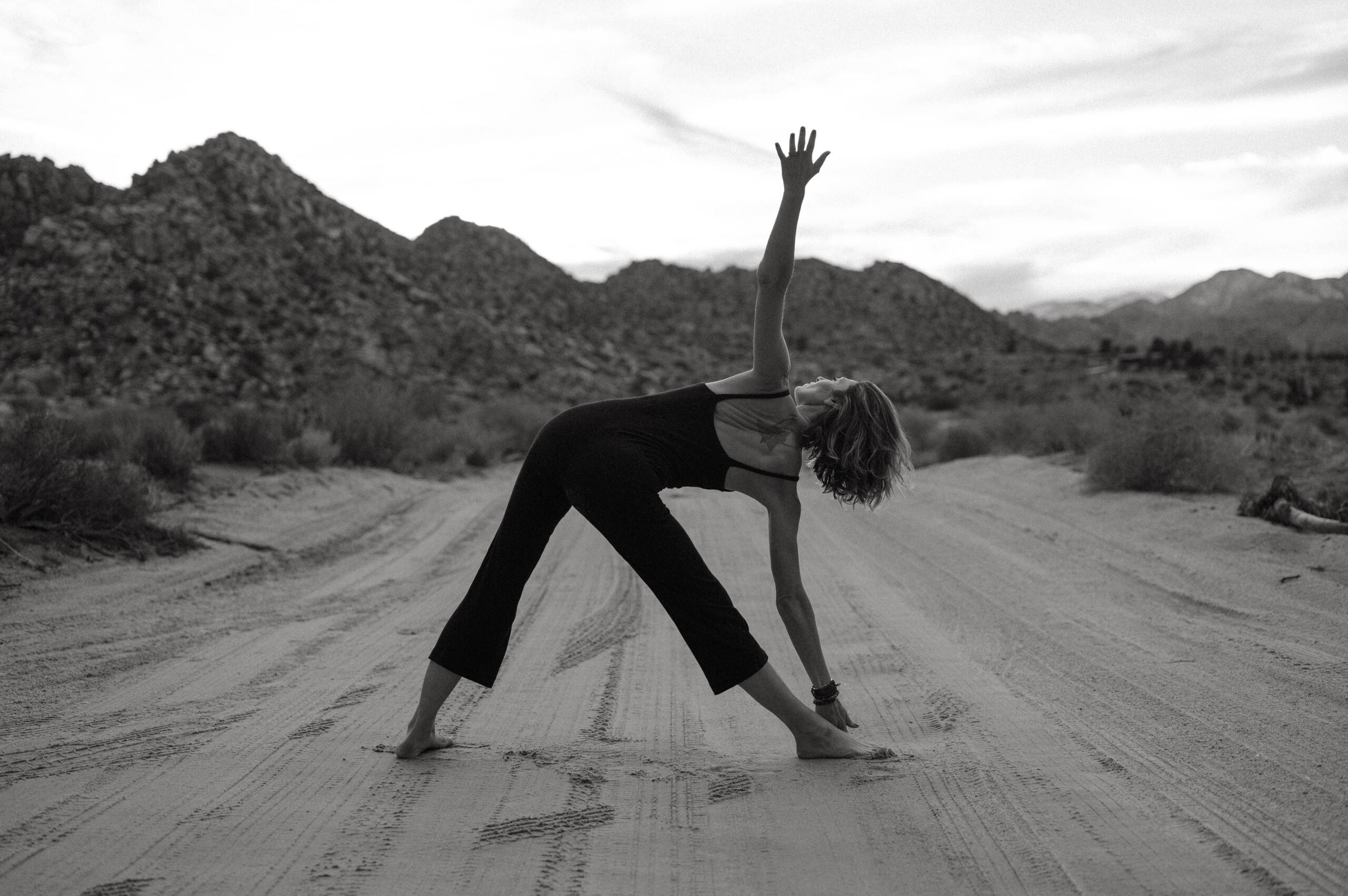 black and white picture of a woman on a sandy beach in a yoga pose facing away from the camera