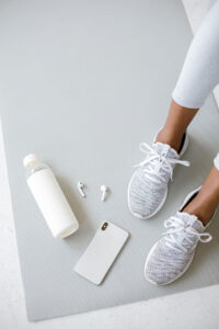 picture of a woman sitting on a white yoga mat with her phone and water bottle
